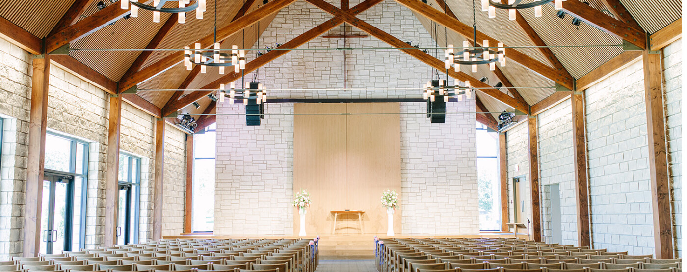 Inside the Chapel at Bent Tree: wood beams and tall windows, daylight across the room, and rows of wooden chairs facing a simple stage.