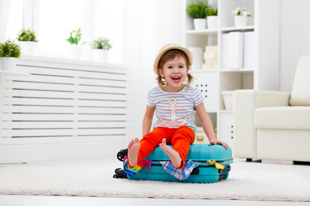 happy-excited-girl-sitting-atop-packed-suitcase