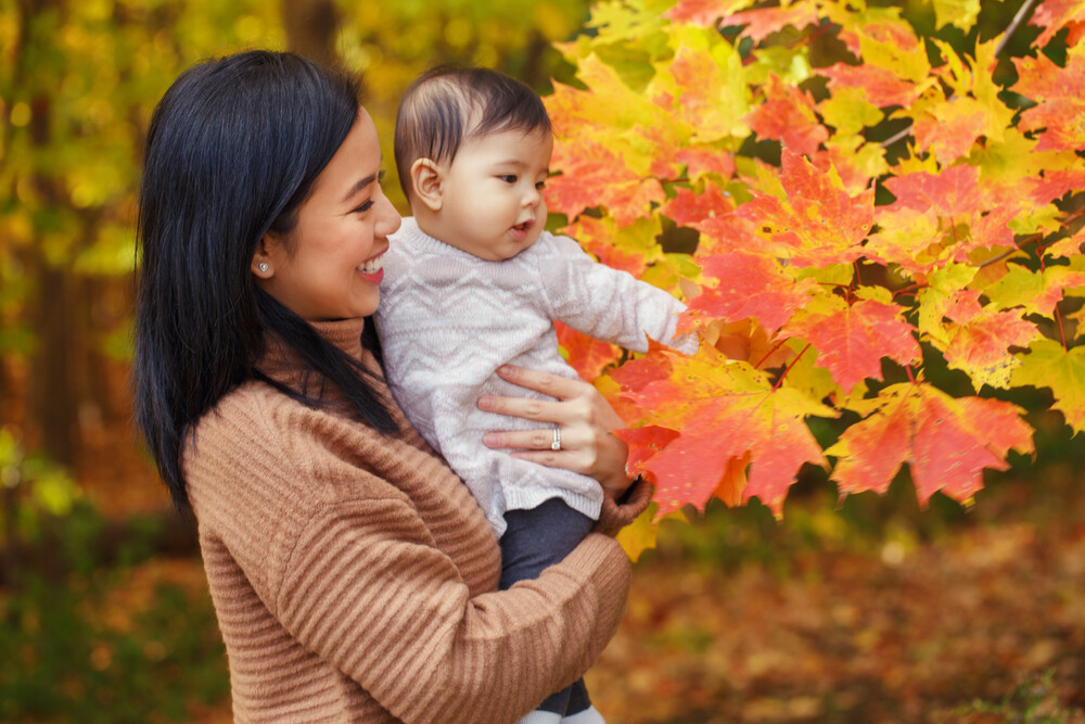 mom-holding-young-daughter-to-touch-fall-leaves
