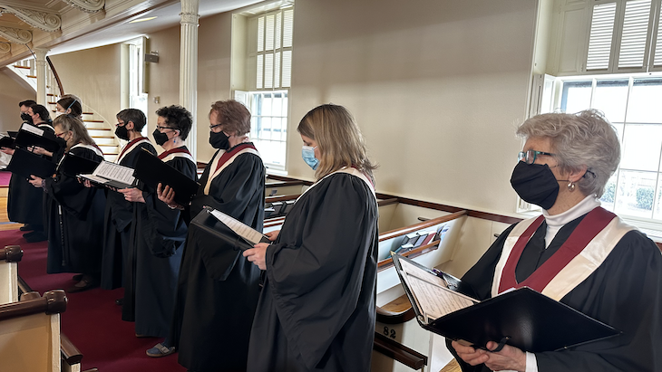 Choir members prepare to sing in the sanctuary, wearing masks