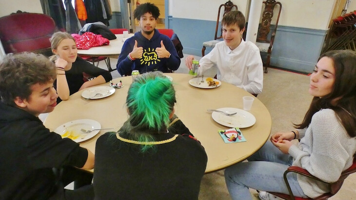 A teen gives a thumbs up sign while eating with other youth