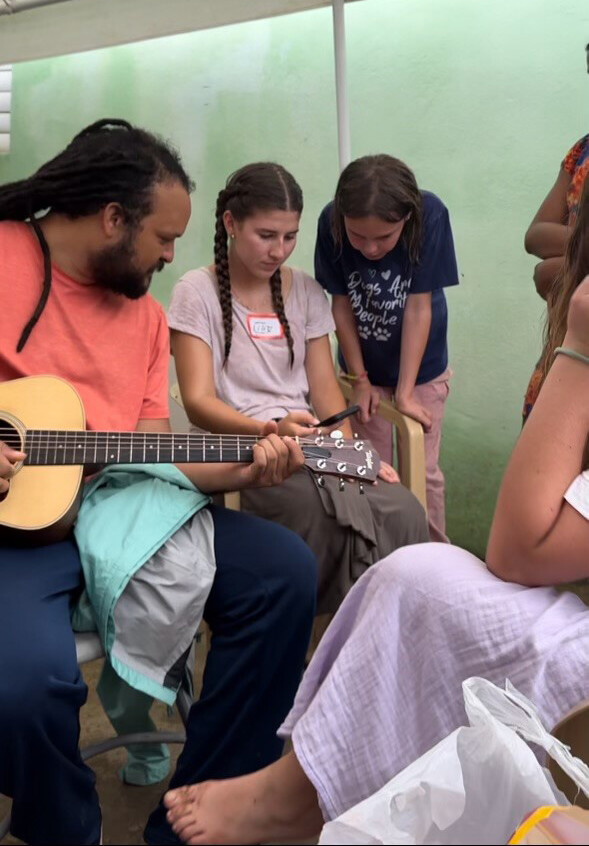 a man playing guitar while two girls look at a phone for lyrics to the song