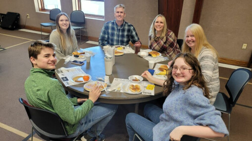 teens and parents smiling and eating breakfast food at a round table in a meeting hall