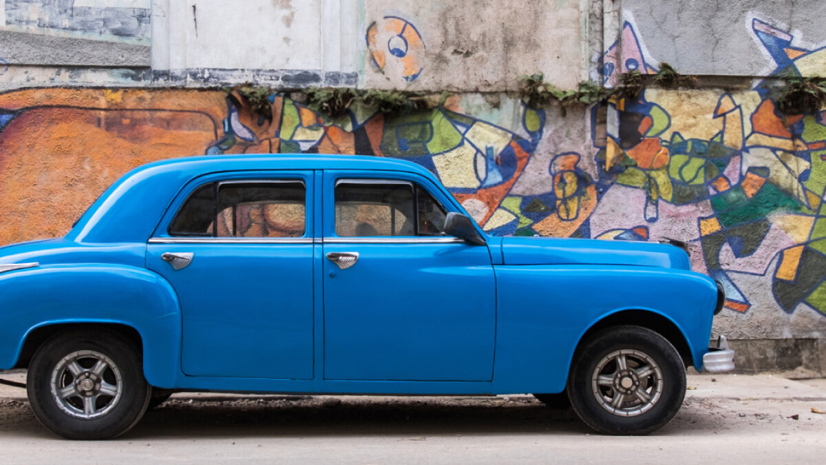 A blue car parked in front of a painted mural wall
