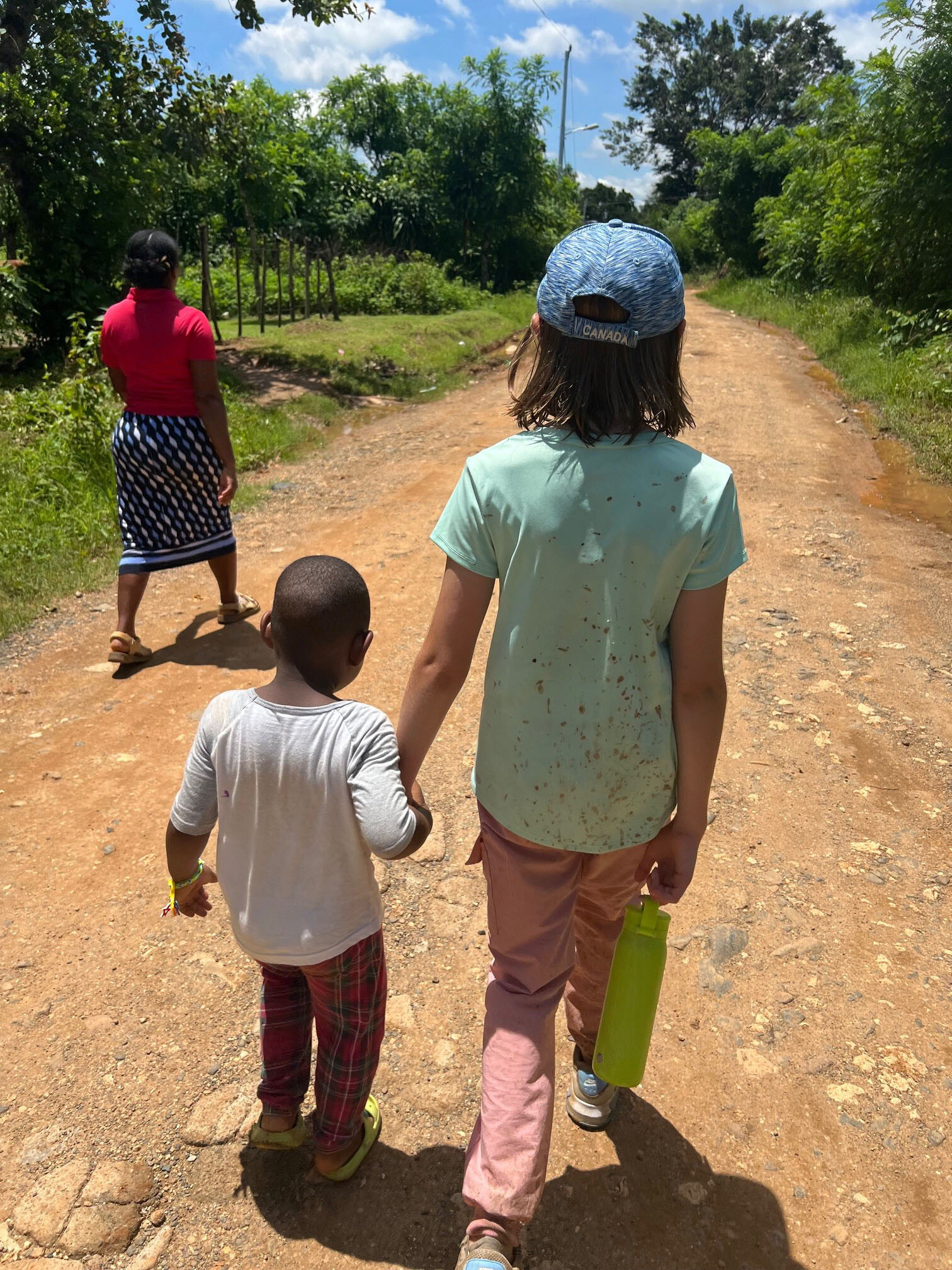 photo of young american girl holding the hand of a small dominican boy as they walk down a dirt path