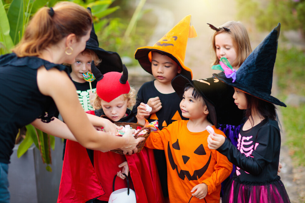 lady-passing-out-candy-to-group-of-eager-kids-on-halloween
