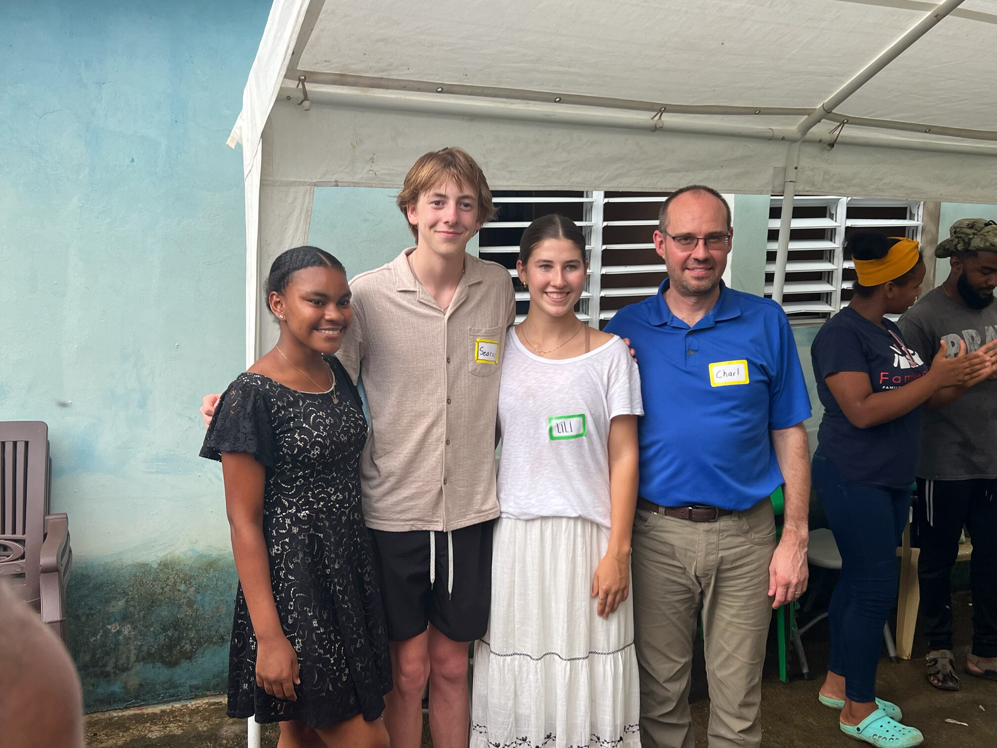 a group of americans including a middle-aged man, a young man and a young woman pose for a photo with a young dominican girl under a tent