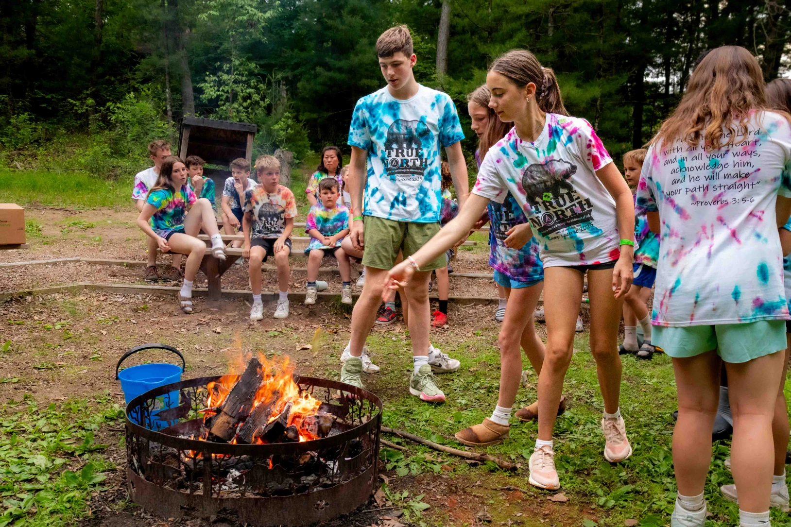 Teens wearing tie-died shirts toss paper with their written fears into a fire at Camp Lake Lucerne