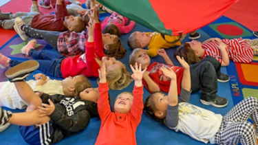 kids laying on ground under a suspended parachute