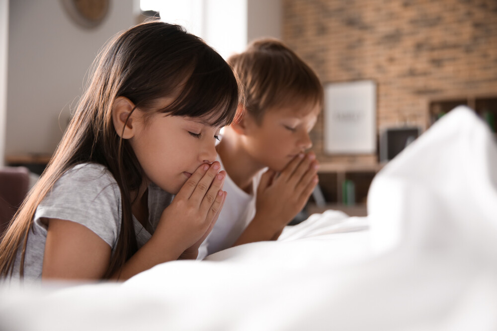 children-praying-together-near-bed-at-home