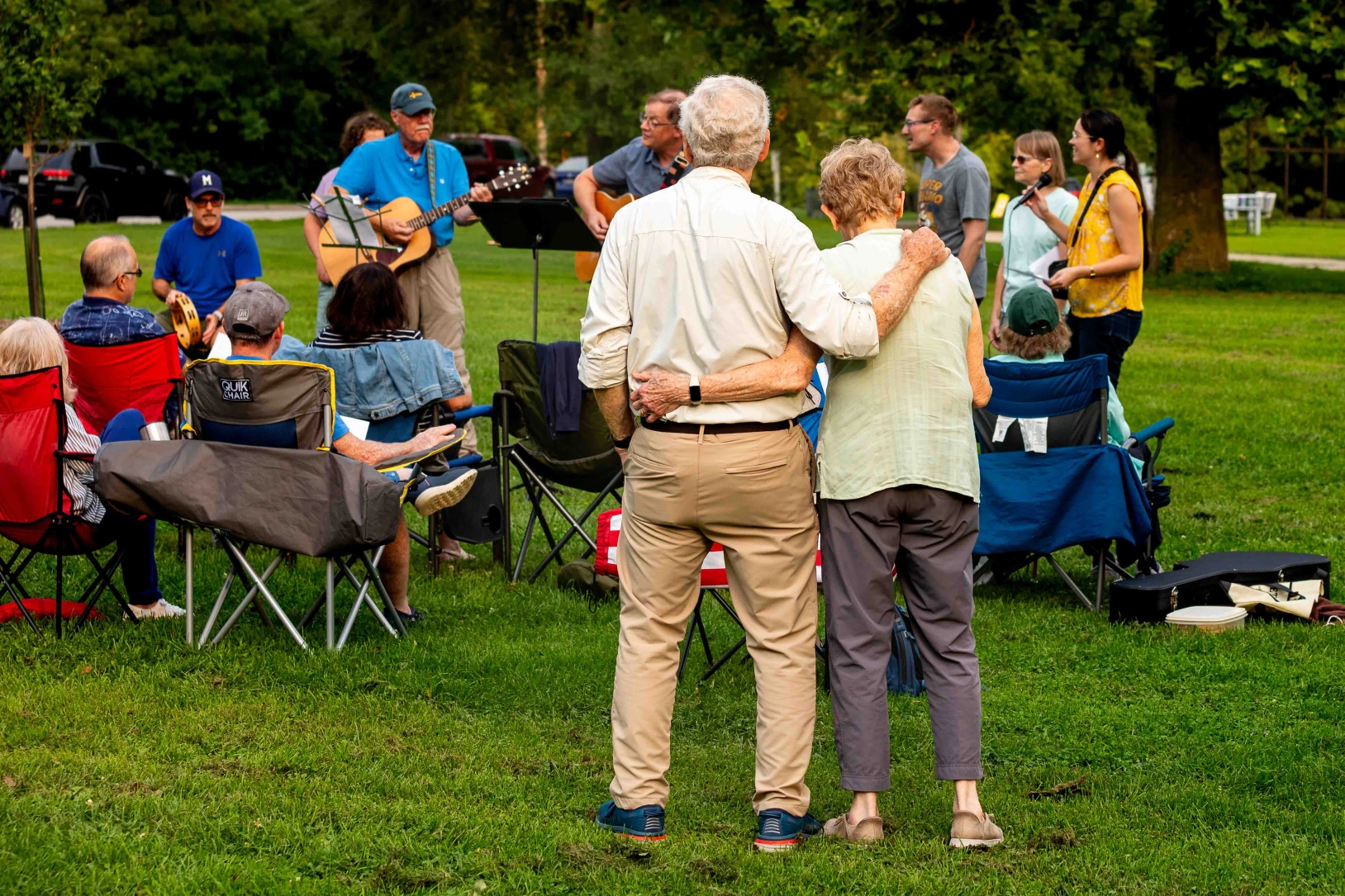 A couple embrace while standing at a contemporary service in a park.