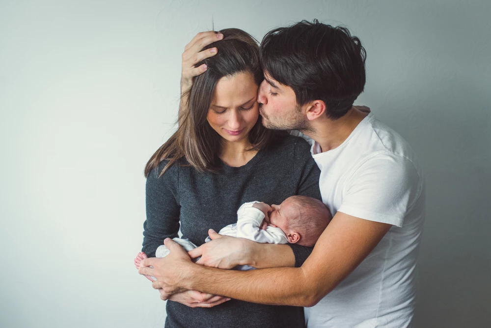 new-young-dad-kisses-his-wife-holding-newborn