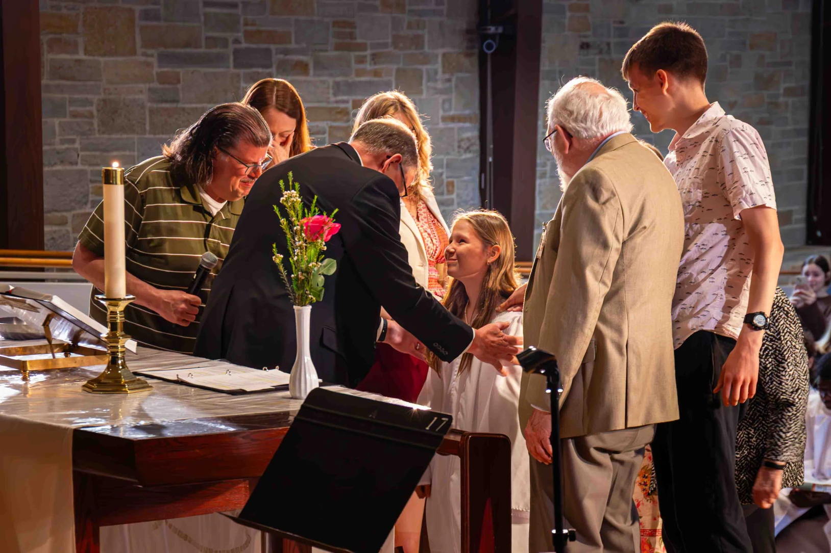 A teen girl surrounded by family  kneels at the altar during during her confirmation.