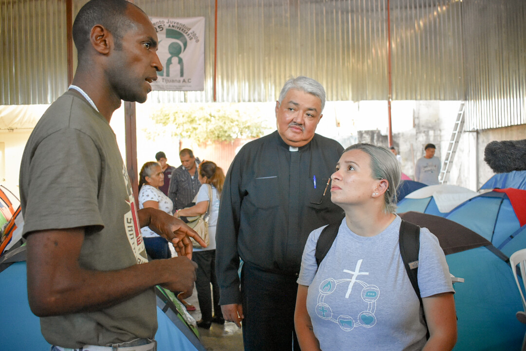 Emma Escobar and Rev Miguel Balderas from the BWC speaking to an assylum seeker at a migrant shelter full of tents in Tijuana
