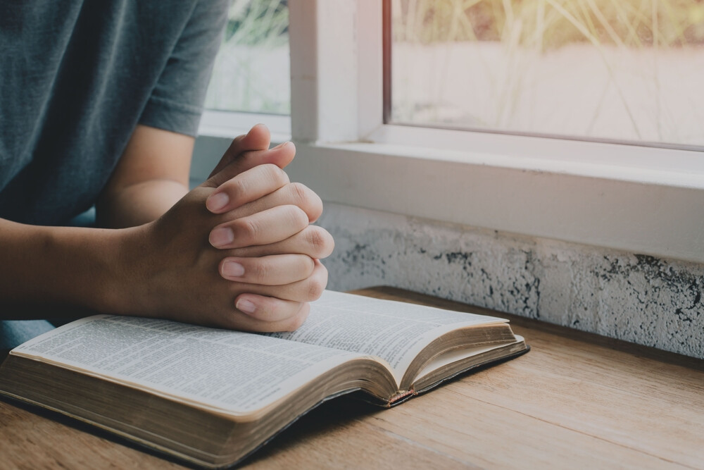 close-up-of-hands-clasped-in-prayer-over-an-open-Bible