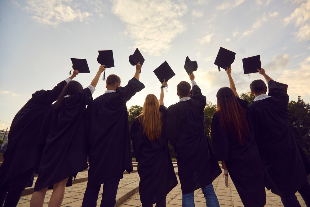 back-view-of-happy-high-school-grads-holding-up-caps