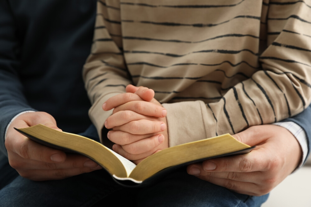 closeup-of-parent-holding-child-praying-and-reading-the-Bible