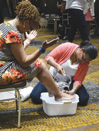 The Rev. Dawn Hand, kneeling, washes the feet of the Rev. Johnsie Cogman. 
