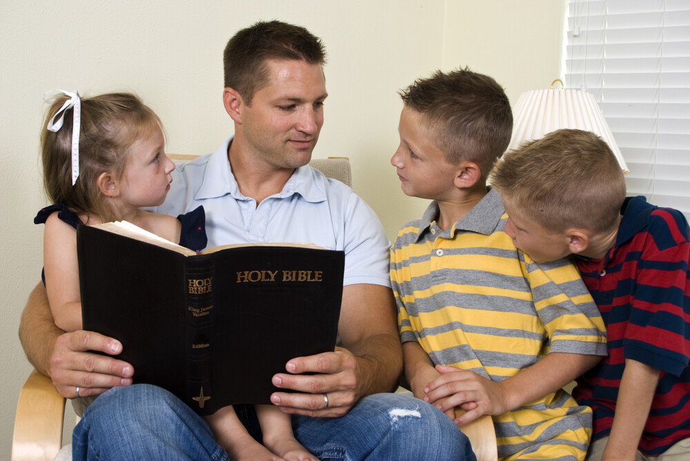a-father-reads-to-his-three-young-children-from-the-holy-Bible