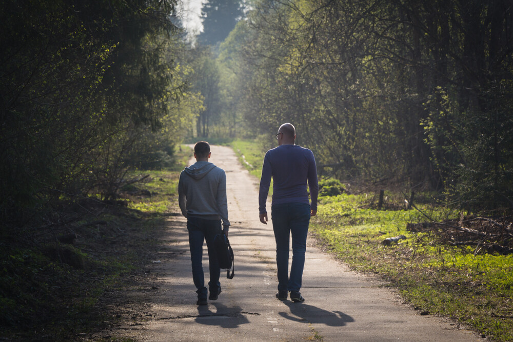 back-view-of-two-adult-male-friends-walking-and-talking-on-a-path