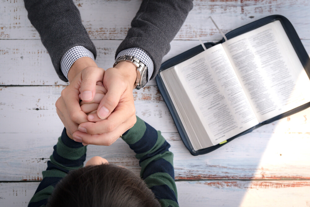 top-view-of-open-Bible-father-and-young-son-holding-hands-praying