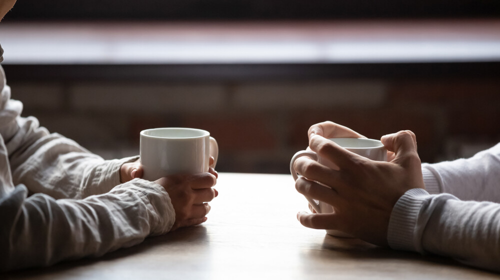 close-up-of-man-and-woman-sitting-in-cafe-holding-warm-coffee-cups