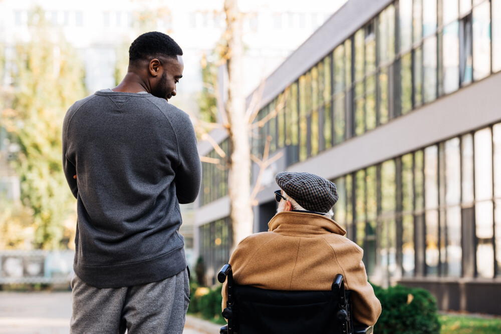 young-black-man-walking-next-to-elderly-disabled-man-in-wheelchair