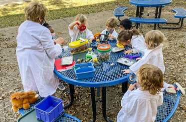 kids outdoors studying bugs with magnifying glasses